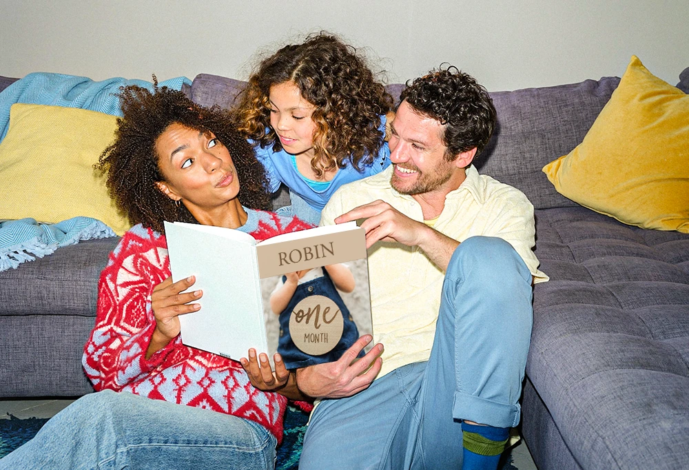 Familie sitzt gemeinsam auf dem Sofa und schaut ein Fotobuch mit Erinnerungen durch.