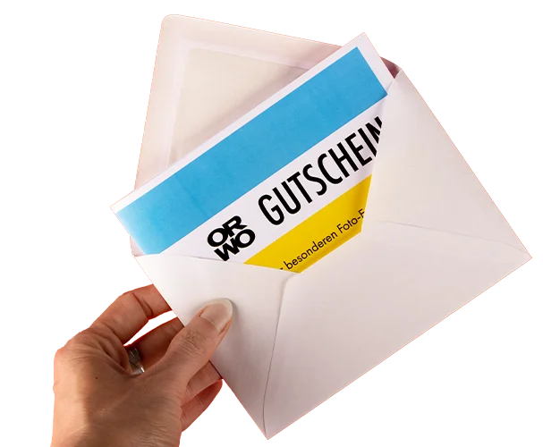 Hand hält weißen Umschlag mit ORWO Geschenkgutschein in Blau und Gelb.