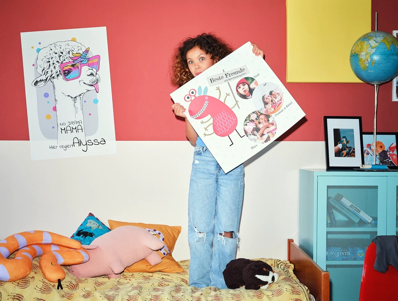 Kind im Kinderzimmer auf Bett mit Kuscheltieren stehend mit lustigem Posterdruck in der Hand hochhaltend mit 