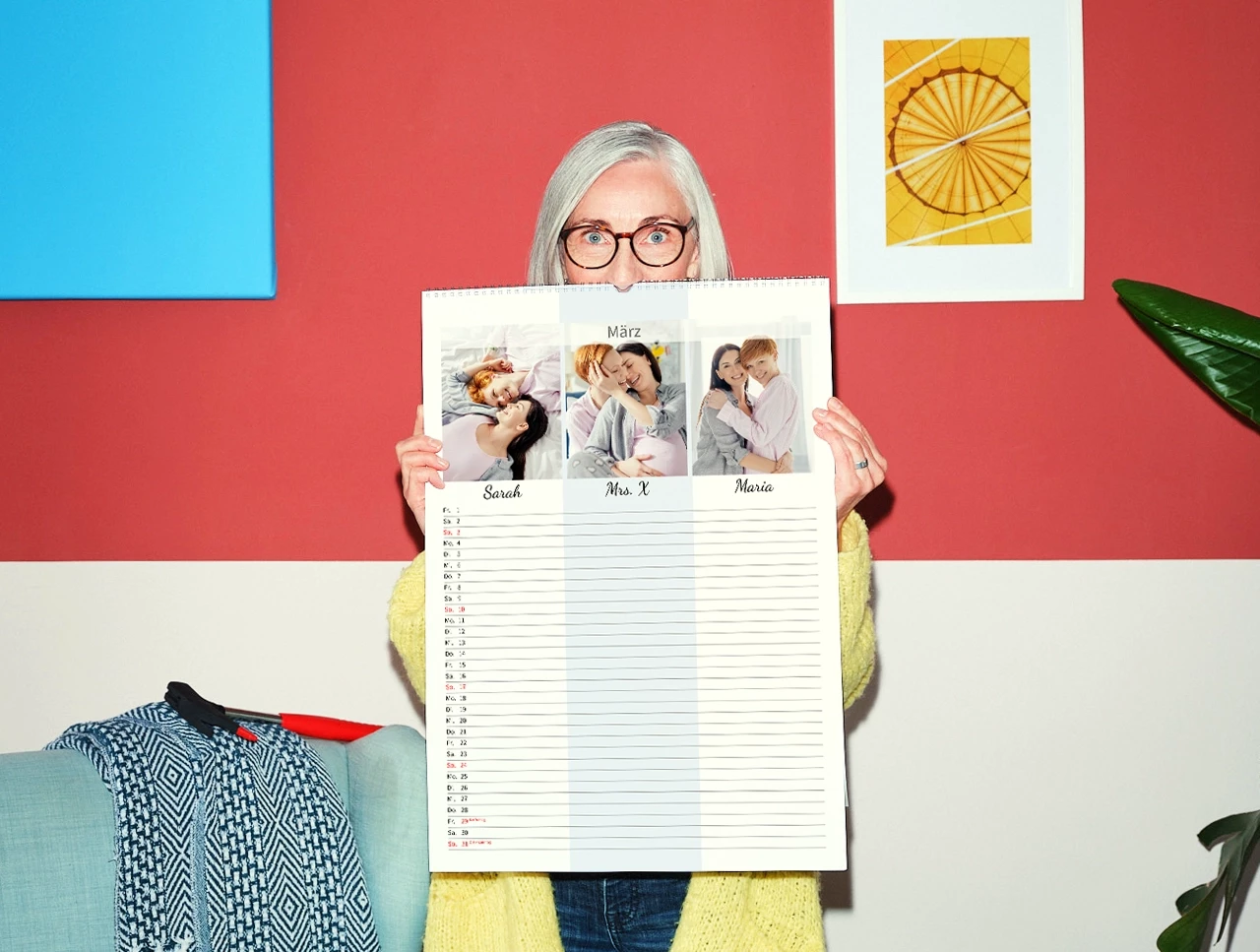 Eine weißhaarige Frau im gelben Strickmantel hält einen großen Terminkalender vor sich, der zeigt, wie du deinen Fotokalender selbst gestalten könntest.