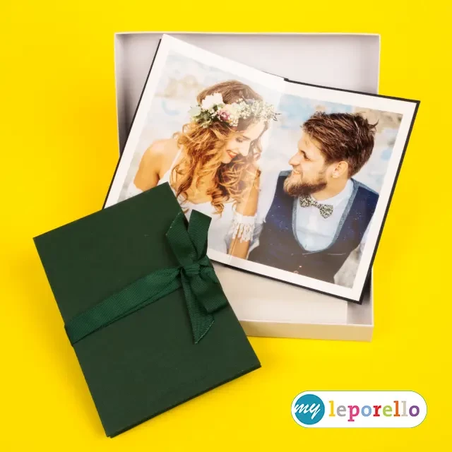 Foto Leporello, dunkelgrün, mit Geschenkverpackung Grünes Faltbuch, einmal offen, einmal zugeklappt, liegt lehnend an der weißen Verpackungsbox, die mitgeliefert wird, um das Leporello gut zu verstauen.