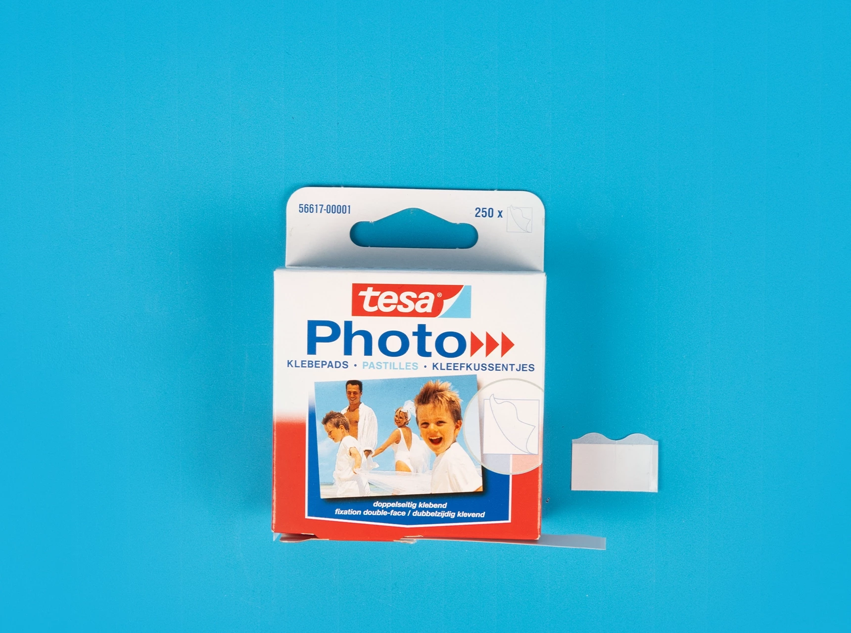 Verpackung der Tesa Photopads mit herausgenommenen Klebepads auf blauem Hintergrund.