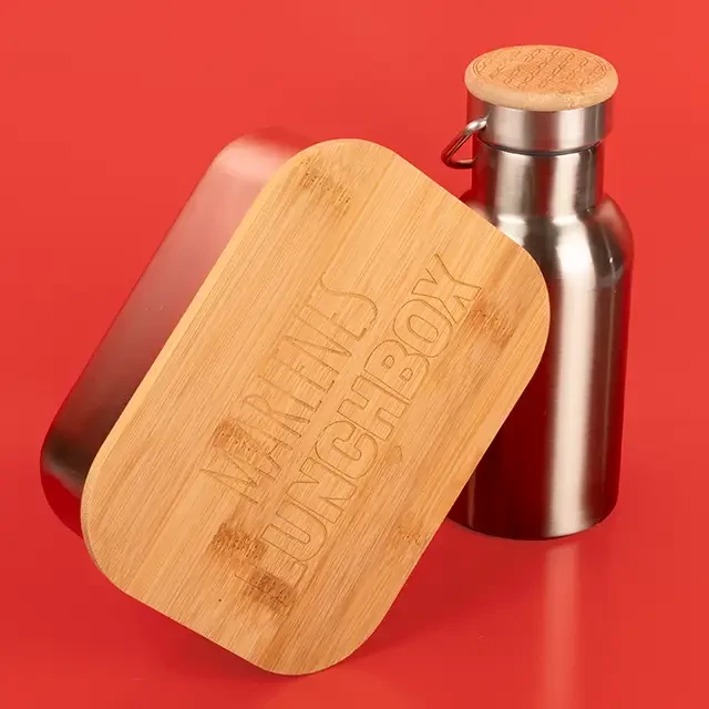 Zu sehen sind zwei unserer Gravur-Produkte. Im Vordergrund steht die Lunchbox. Den Deckel aus Bambus kannst du bei uns mit deinem Namen gravieren lassen.