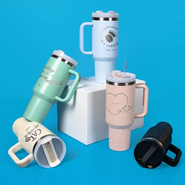 Stanley Cup ähnliche Becher in verschiedenen Farben Drei Thermobecher XXL in Beige, Peach und Mint stehen nebeneinander, ein hellblauer Becher liegt obendrauf.