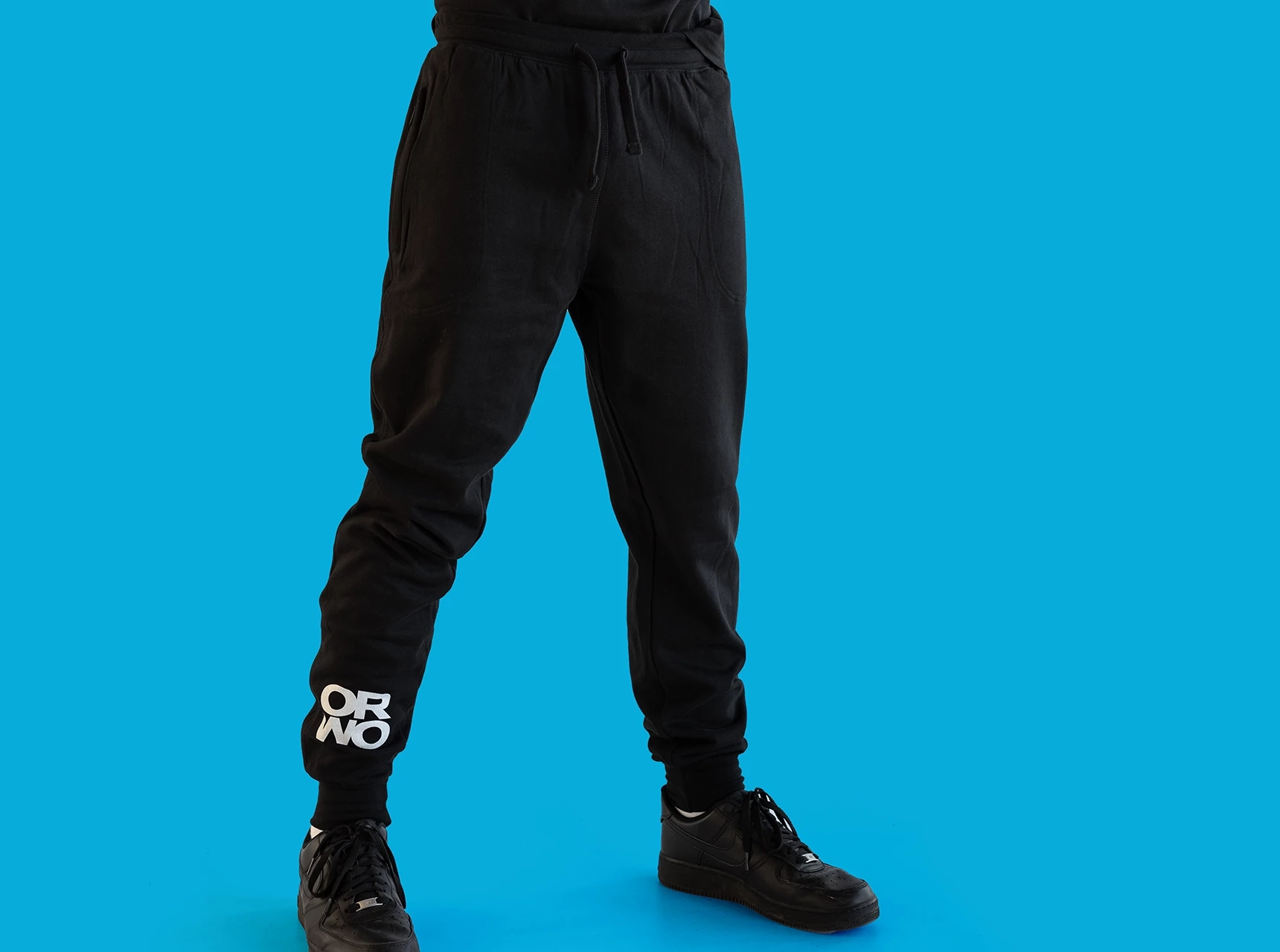 Hier wird die Jogginghose mit ORWO-Print am rechten unteren Bein vor blauem Hintergrund zur Schau gestellt. Die Hose besteht zu 100% aus Bio-Baumwolle.