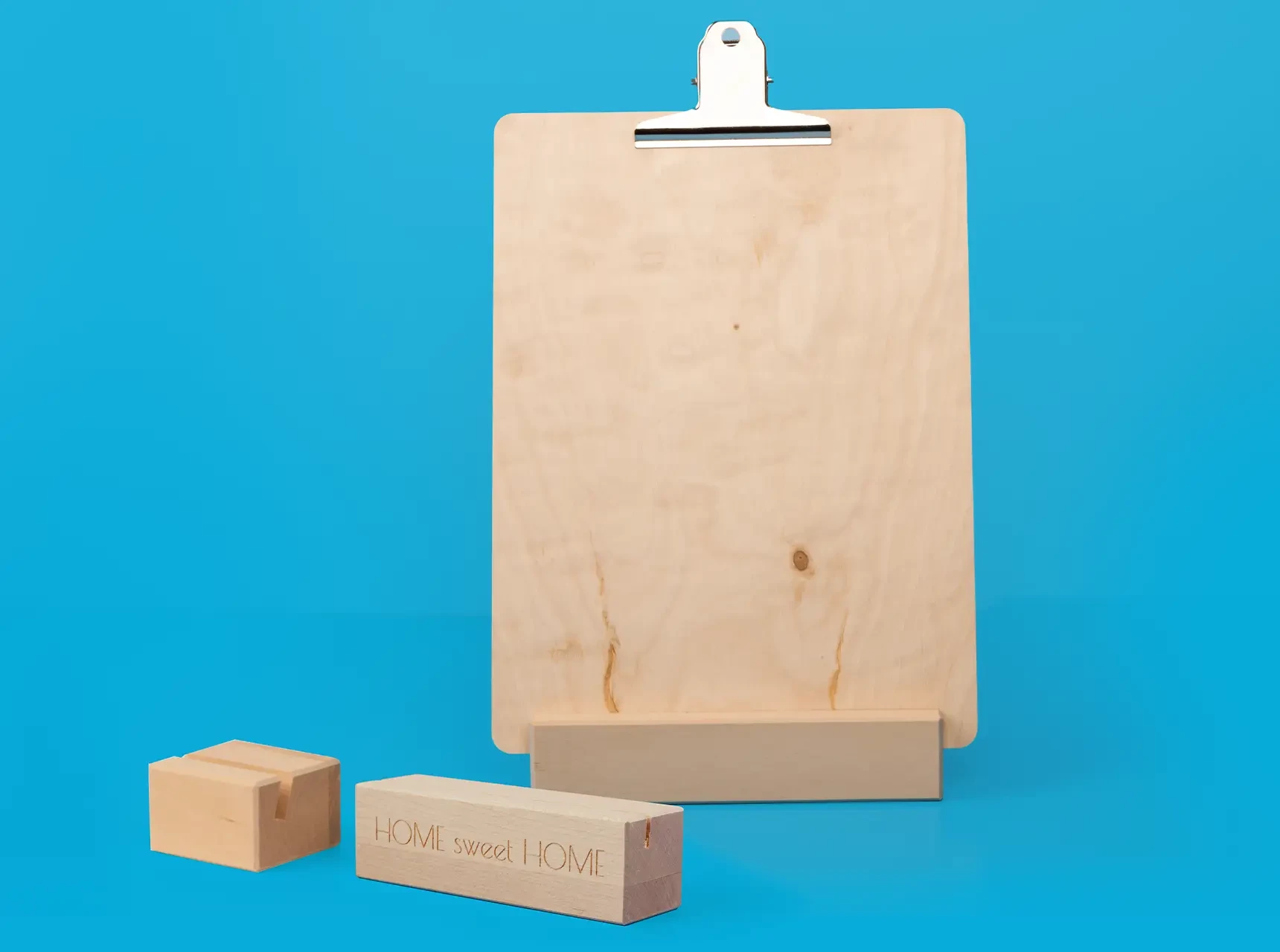Drei Bildhalter-Varianten: zwei Holzfüße mit Nut – einer davon mit Gravur – und ein Klemmbrett mit Metallklemme und Standfuß.