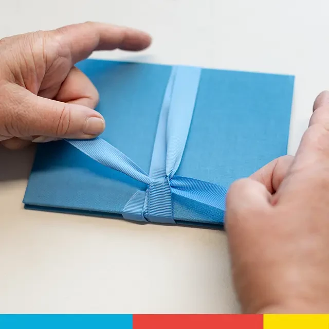 Faltbuch liebevoll zusammengebunden mit Schleife, azurblau Azurblaues Leporello mit Fotos wird liebevoll und sorgsam von fürsorglichen Händen zusammengebunden mit einer farblich passenden Schleife, die es gut zusammenhält.