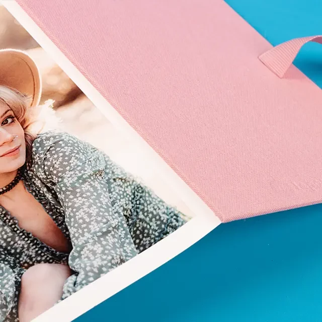Leporello Foto, rosa, selbst gestalten, hochwertig Die untere Ecke eines Leporellos mit Foto bedruckt. Das Leporello ist rosa und liegt aufgeklappt auf blauem Untergrund und präsentiert das Bild einer Dame am Strand.