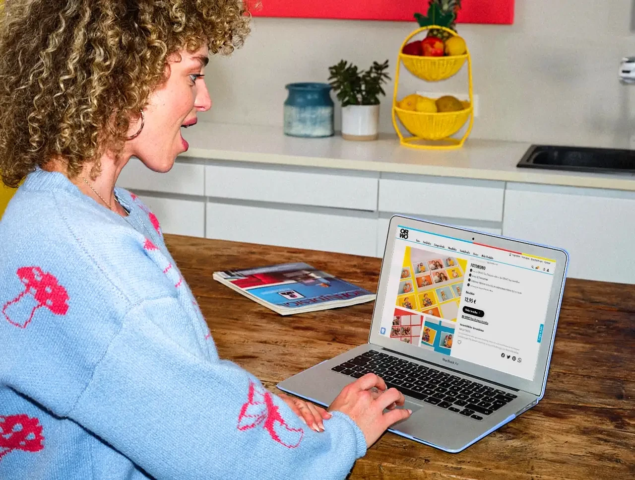 Eine Frau sitzt am Küchentisch vor ihrem Laptop und hat orwo.de geöffnet – auf der Suche nach Fotopuzzle und Memory-Spielen.