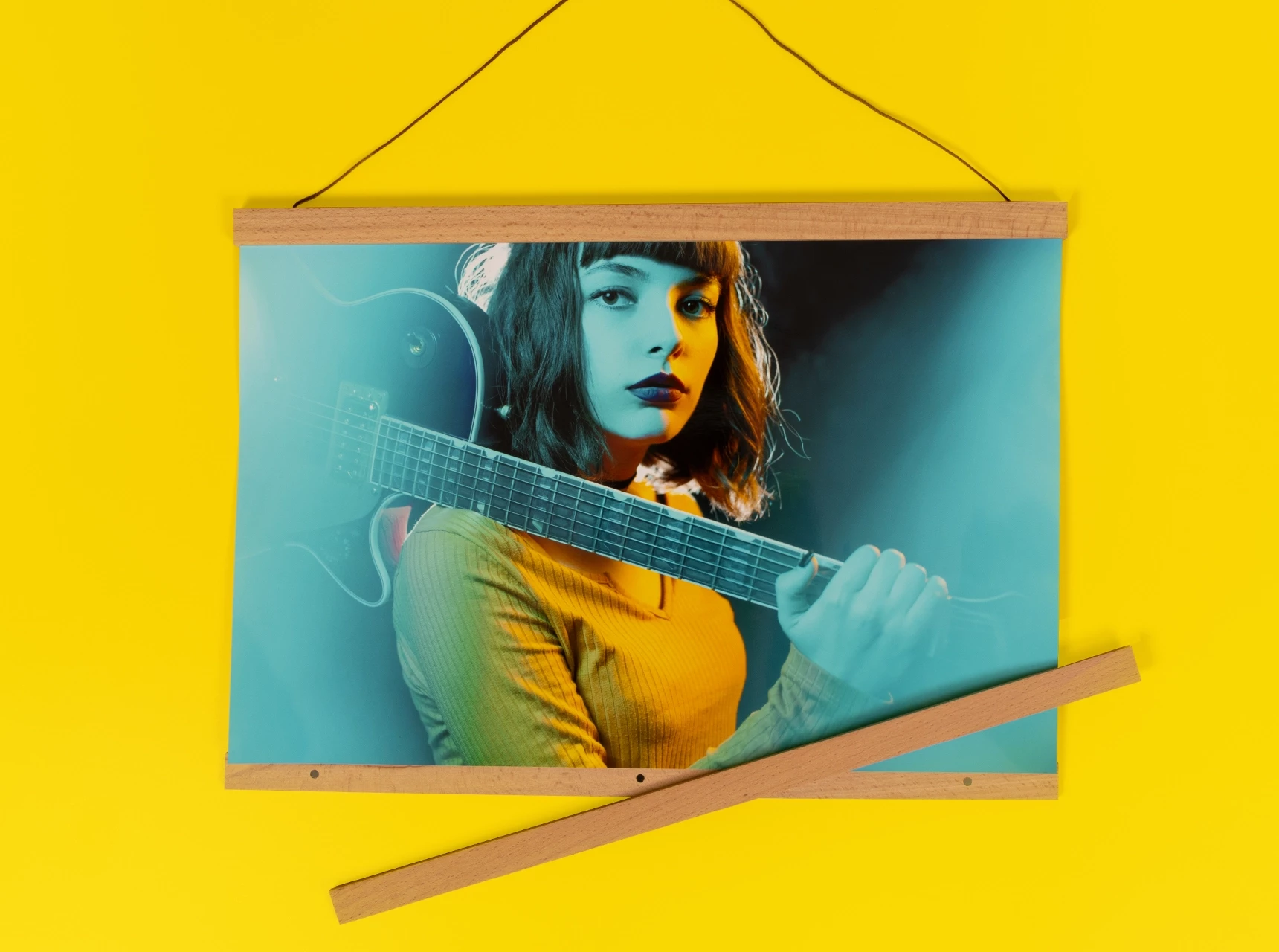 Posterleiste aus Holz mit brauner Kordel, eingerahmt ist ein Poster einer jungen Frau mit Gitarre über der Schulter.