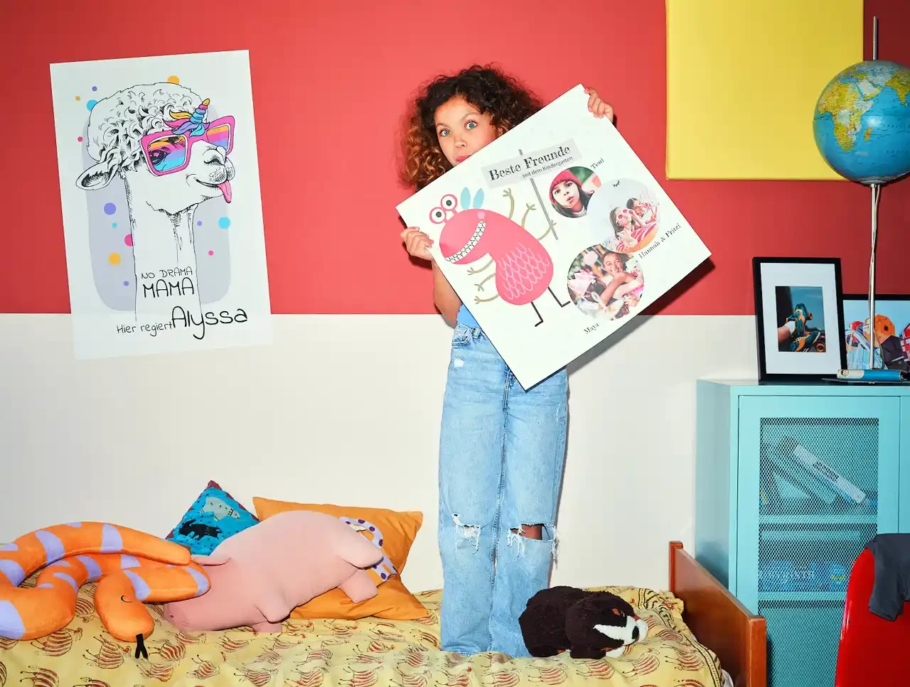 Witzige Poster für das Kinderzimmer drucken Kind steht auf einem Bett mit Kuscheltieren und hält Poster in den Händen. Lass auch du dein Poster drucken!