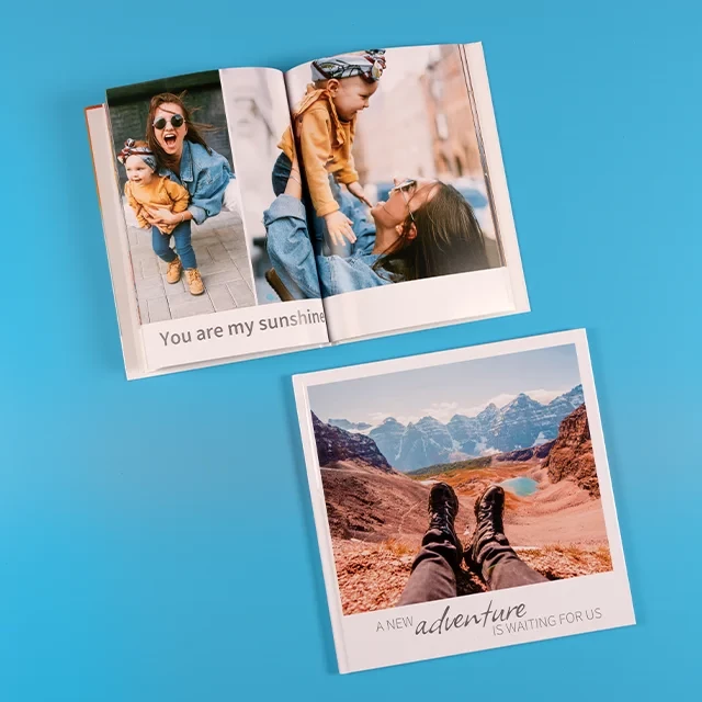 Zwei Fotobücher, ein quadratisches Urlaubs-Fotobuch mit großem Foto und Text und ein aufgeschlagenes, hochformatiges Buch mit Familien-Momenten und passendem Schriftzug. 