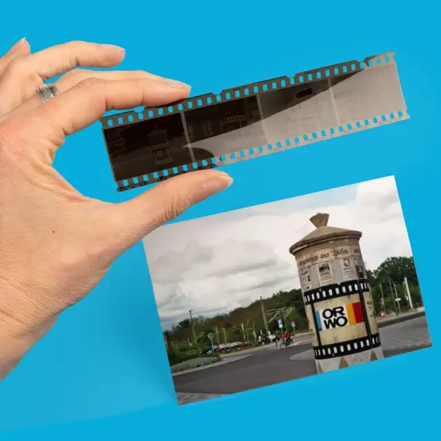 Farbfilm Fuji C41-200/36 für Innen- und Außenaufnahmen Das fertige Bild nach der Entwicklung deines Analogfilms zeigt eine Litfaßsäule mit ORWO-Logo. Der dazugehörige Negativstreifen wird von einer Hand ins Bild gehalten.