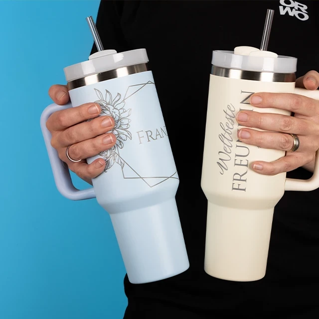 Stanley Cup inspirierter Becher aus Edelstahl, 40 OZ Becher im Stanley Cup Stil, der mit der Öffnung nach vorn zeigt, daneben liegen der Deckel und ein Strohhalm.