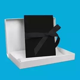 myLeporello in Schwarz – schlicht & zeitlos Elegantes myLeporello in Schwarz mit passender Schleife, arrangiert in offener, weißer Verpackung vor blauem Hintergrund.