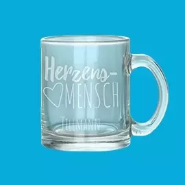 Deine Glastasse mit individueller Gravur Transparente Glastasse mit eingraviertem Motiv "Herzensmensch". In Szene gesetzt vor einem blauen Hintergrund.
