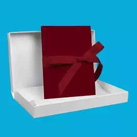 myLeporello in Weinrot – stilvoll und persönlich Geöffnete Geschenkbox in Weiß, darin ein geschlossenes myLeporello mit weinrotem Leineneinband und passender Schleife. Präsentation vor blauem Hintergrund.