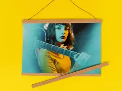 Posterleiste aus Holz mit Magnetverschluss – inkl. Aufhängung mit Kordel Posterleiste aus Holz mit brauner Kordel, eingerahmt ist ein Poster einer jungen Frau mit Gitarre über der Schulter.