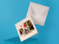 Quadratische Fotoklappkarte mit Weihnachtsmotiv – personalisierte Karte mit Foto einer Frau und ihres Hundes in Weihnachtsstimmung, daneben passender Umschlag auf blauem Hintergrund.