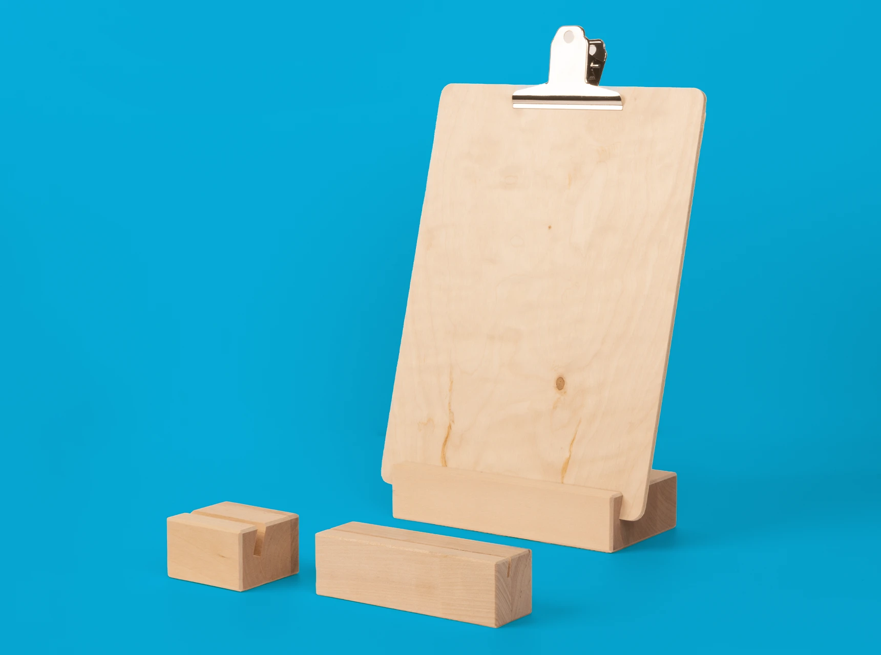 Zwei schlichte Fotohalter aus hellem Holz mit Schlitz für Bilder sowie ein Fotohalter mit Klemmbrett-Funktion auf blauem Hintergrund