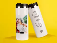 Zwei weiße Thermobecher auf gelbem Hintergrund – einer mit Foto eines Paares, der andere mit dem gravierten Schriftzug „Emilia“ und Herzsymbol.