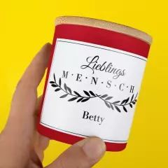 Eine Hand hält eine Duftkerze personalisiert. Das Etikett zeigt den Schriftzug „Lieblingsmensch“ und den Namen „Betty“.