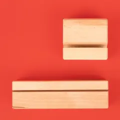 Zwei minimalistische Fotohalter aus naturbelassenem Holz mit eingefrästem Schlitz auf rotem Hintergrund, geeignet zum Aufstellen von Fotos oder Karten