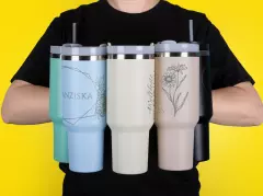 Fünf große Thermobecher in Stanley Cup Optik, die vor dem Körper gehalten werden, mit Henkel und Strohhalm. In fünf Farben erhältlich.