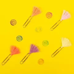 Büroklammern – verspielte Varianten mit Püscheln und farbigen Spiralen für kreative Ordnung Fünf klassische Büroklammern mit kleinen, bunten Püscheln sowie mehrere spiralförmige Büroklammern in kräftigen Farben – locker verteilt.