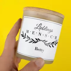Duftkerze, personalisiertes Etikett, hochwertiges Glas Eine Hand hält eine Duftkerze personalisiert. Das Etikett zeigt den Schriftzug „Lieblingsmensch“ und den Namen „Betty“.