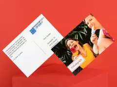 ORWO Postkarte zum Selbstgestalten und Direktversand, Vorderseite mit fröhlichen Urlaubsmotiven von jungen Frauen beim Eisessen, Rückseite mit Adresse, Briefmarke und persönlichem Gruß, moderne Fotopostkarte vor rotem Hintergrund.