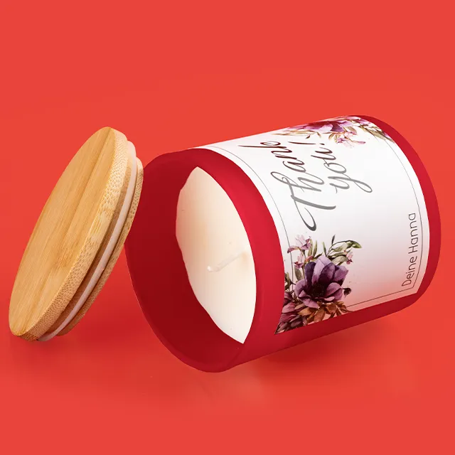 Duftkerze, personalisiert, mit Bambusdeckel Eine Duftkerze, personalisiert mit dem Spruch „Thank You“ liegt auf einer roten Fläche. Der Bambusdeckel lehnt an der Kerze.