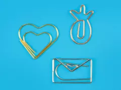 Büroklammern – ausgefallene Formen wie Herz, Ananas und Briefumschlag in edlen Metallic-Tönen Drei besondere Büroklammern in Form eines goldenen Herzens, einer bronzefarbenen Ananas und eines silbernen Briefumschlags, stilvoll arrangiert.