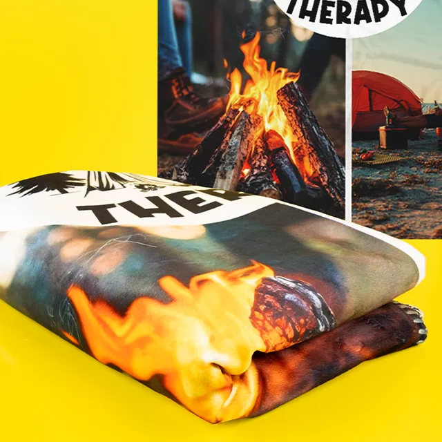 Gefaltete Fotodecke mit Lagerfeuer-Motiv und warmen Farben.