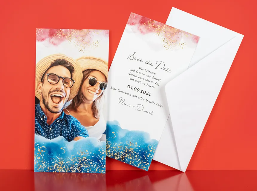 ORWO Fotokarten im Hochformat mit persönlichem Foto eines lachenden Paares, gestaltet als Save-the-Date-Karte mit modernem Aquarell-Design, Einladungstext und weißem Umschlag vor rotem Hintergrund.