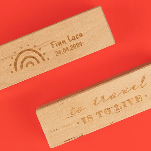 Zwei gravierte Holz-Fotohalter mit individuellen Motiven und Texten, einer mit Regenbogen und Namen „Finn Luca“, der andere mit der Gravur „to travel is to live“.