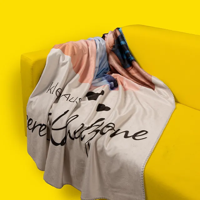 Fotodecke mit persönlichem Schriftzug liegt über gelbem Sofa drapiert.
